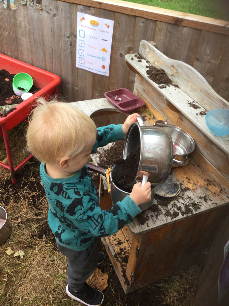 Child tipping mud into saucepan