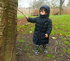 Child playing outside, touching a tree with a stick