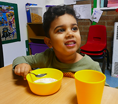 Child holding a spoon, eating from a bright yellow bowl