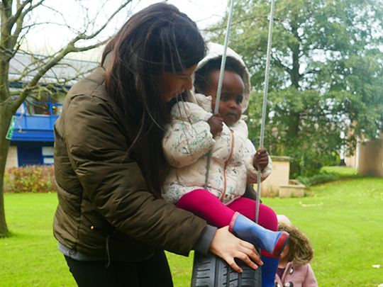 Nursery staff with child playing on swing